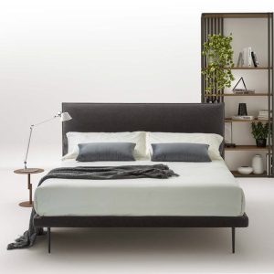 Elegante letto matrimoniale con testiera imbottita in tessuto grigio, abbinato a luci da lettura minimaliste, in una stanza moderna e raffinata, perfetta per arredare camere da letto di design.