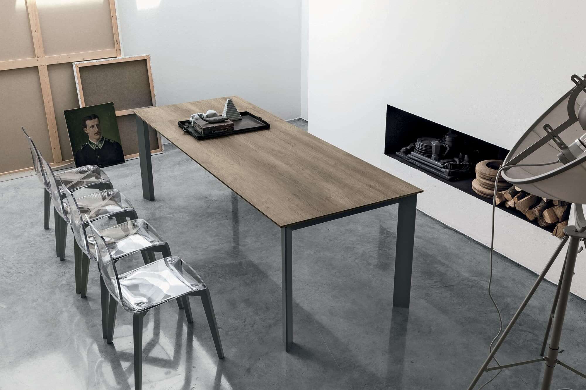 Tavolo in legno di design con sedie trasparenti, ambiente moderno con pareti bianche e camino, arredamento di alta qualità per living e ufficio, marca Alpe Arredi.