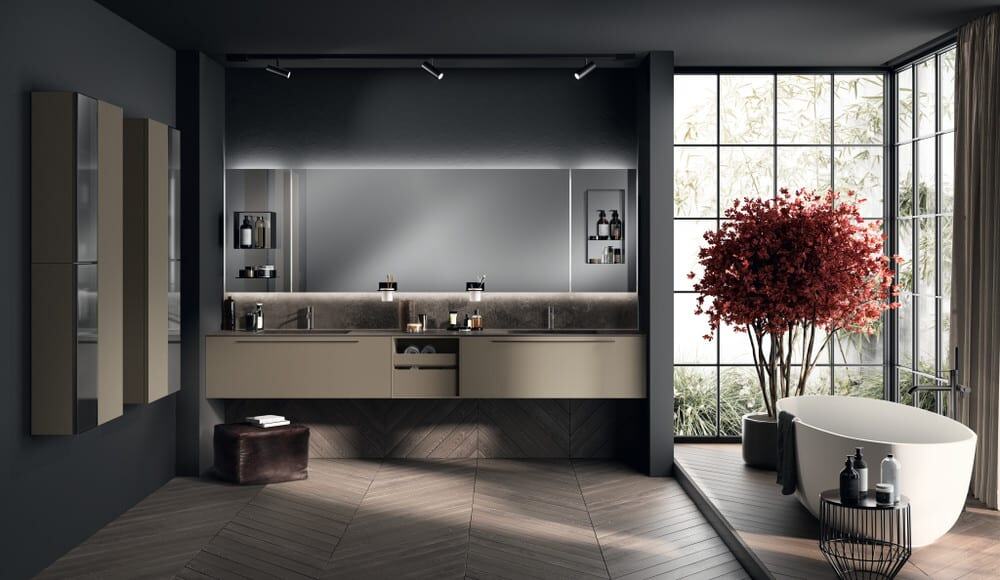 AQUO_pag_18_19 Elegante bagno con mobili su misura, specchio grande e atmosfera moderna, arricchito da una pianta di acero rosso e vasca da bagno freestanding, ideale per ambienti di lusso e design di alta qualità.