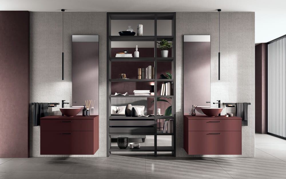 AQUO_pag_26_27 Elegante arredo bagno con doppi lavabi, mobili in stile moderno colore bordeaux, scaffalatura divisoria in metallo, dettagli di design contemporaneo, ambiente raffinato e funzionale.