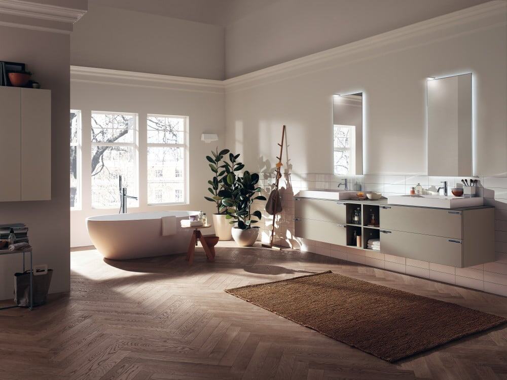 aquo_pag_176_177 Elegante bagno con vasca da libero stile minimalista, grande finestra con vista su alberi, mobili moderni in tonalità neutre, grandi specchi illuminati, piante verdi e dettagli di design raffinato.