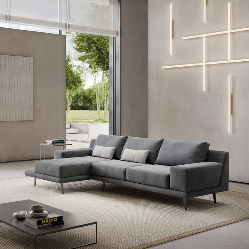 2 Elegante divano grigio in tessuto con design moderno e lineare, ideale per arredi contemporanei, in un soggiorno luminoso con grandi finestre e decorazioni minimaliste di Alpe Arredi.