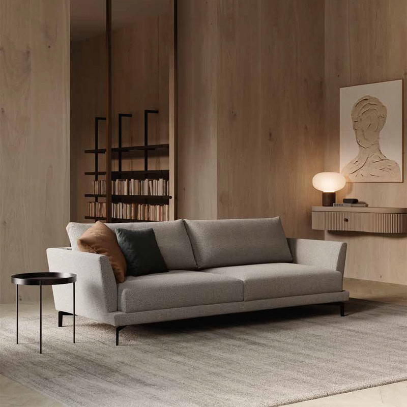 3 Sofà moderno in stile minimalista con rivestimento in tessuto grigio e cuscini decorativi in toni naturali, in un salotto elegante con pareti in legno chiaro.