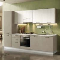 Cucina moderna con ante bianche e piano in laminato chiaro, illuminata da luci sottopensile, con accessori da cucina e lavello integrato.