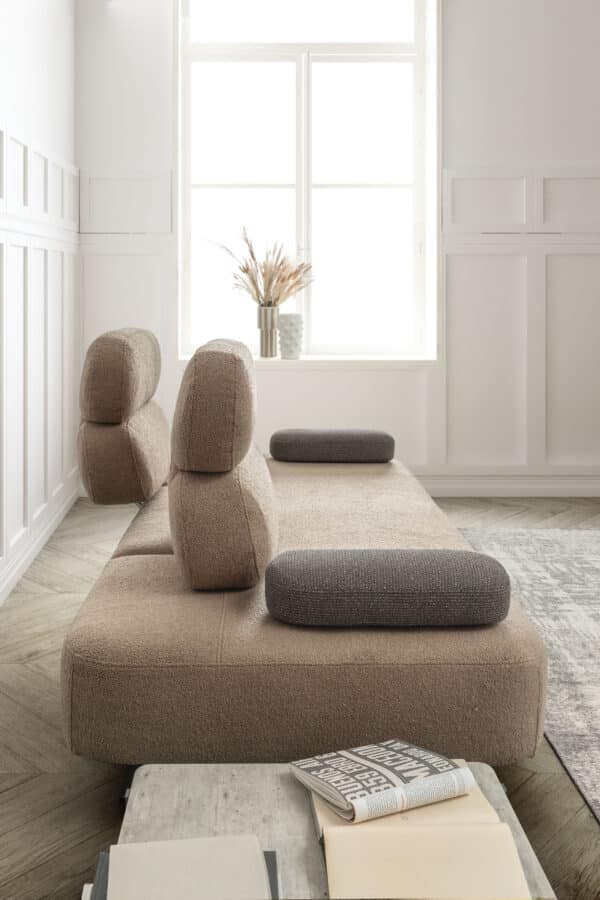 divano-avalon-collezione-divine-5-600x900 Elegante divano beige con schienali regolabili e cuscini grigi in tessuto, ambientazione moderna con luce naturale, ideale per interni di design made in Italy.