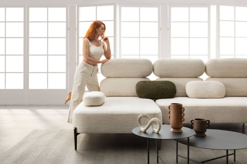 divano-avalon-collezione-divine-8-1000x667 Elegant soggiorno con divano modulare in tessuto chiaro, decorazioni moderne e grandi vetrate che lasciano entrare tanta luce naturale, arredamento di design per ambienti living di alta qualità.