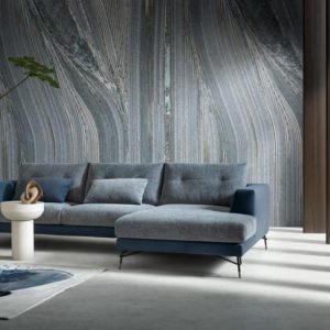 Elegante divano moderno in tessuto grigio e blu in un soggiorno raffinato con pareti in marmo e pannelli in legno, design di alta qualità di Alpe Arredi.