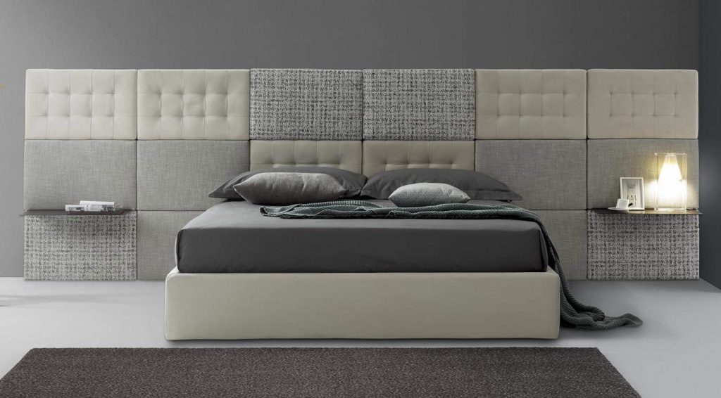 Letto matrimoniale con testata imbottita modulare in tessuto e velluto, notte con lampada da tavolo e cornice foto, camera elegante e moderna.
