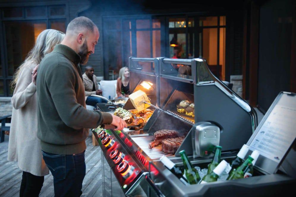 PRO825RSBIPSS-3-Web-Gallery-06-Prestige-Pro825-3-Life-Man-and-Woman-Grilling-Dusk-On-Deck Fiorentina di carne di alta qualità grigliata su barbecue all'aperto in un ristorante elegante. Ambiente conviviale e sofisticato, perfetto per cene e feste con amici e famiglia.