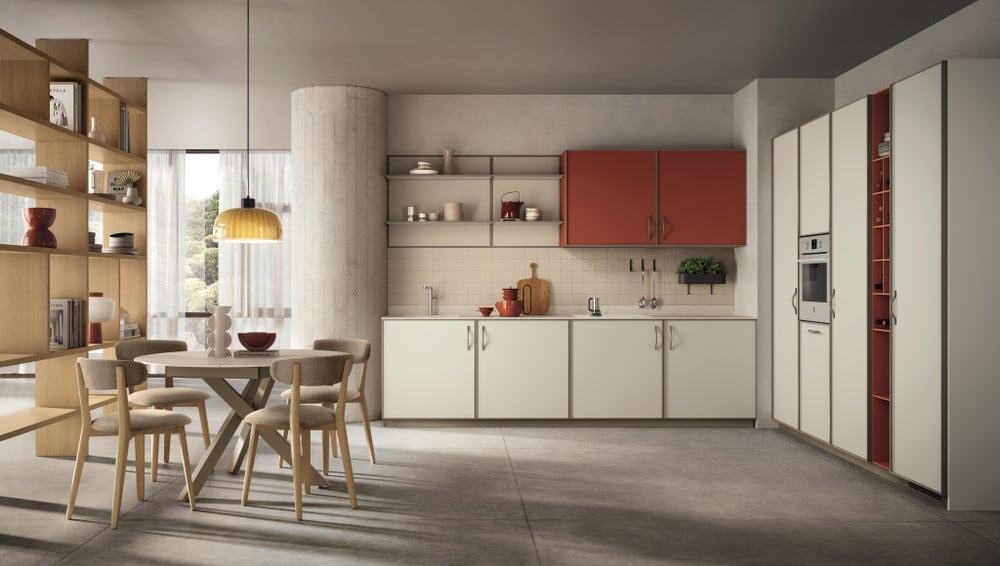 Jeometrica_pag_30_31 Armadio cucina moderno con ante bianche e dettagli rossi, zona pranzo con tavolo rotondo e sedie in stile minimale, soluzione di arredamento elegante e funzionale, perfetta per spazi raffinati.