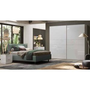 Lettiera moderna in stile minimalista con grande armadio a soffietto bianco e letto imbottito verde con cuscini decorativi, in camera con grande finestra e illuminazione diffusa.