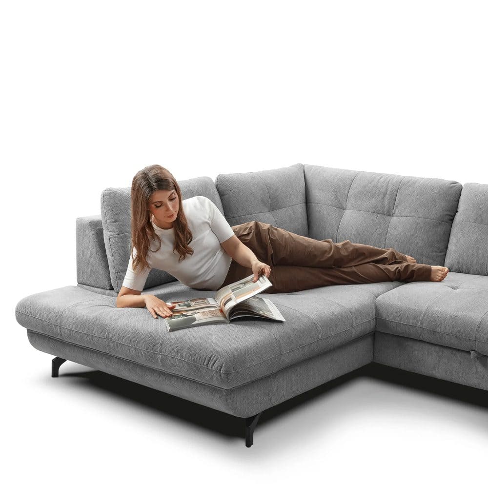 9 Sofa soggiorno moderno in tessuto grigio con donna che legge distesa sul divano. Mobili di alta qualità per arredi eleganti e funzionali, perfetti per salotti contemporanei.
