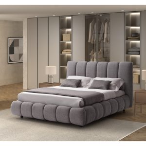 Letto imbottito grigio con testiera alta in una camera moderna con armadiature a muro e illuminazione integrata.