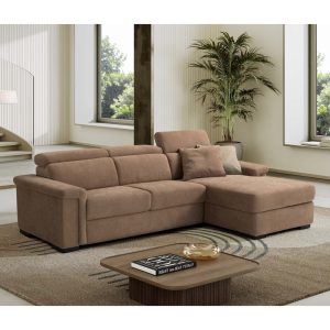 Divano angolare in tessuto beige in un soggiorno luminoso con grandi finestre e piante verdi.