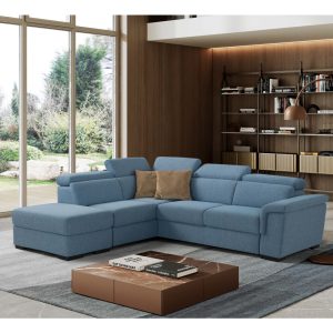 Divano angolare moderno in tessuto blu in soggiorno con grandi finestre e libreria a parete in legno chiaro.