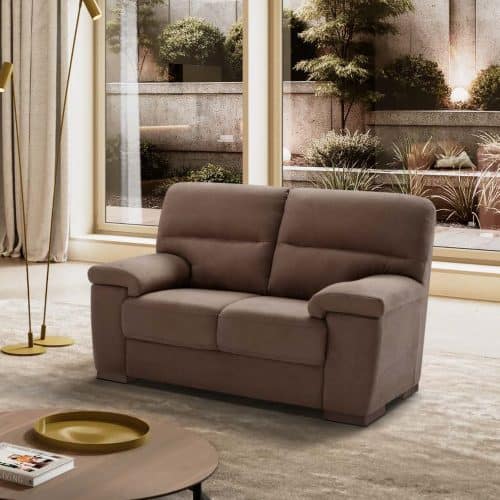 Divano 2 posti GIUDY in tessuto morbido color taupe in soggiorno luminoso con grandi finestre e vista sul giardino.