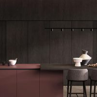 Cucina moderna con ante in legno scuro e piano in tonalità rosa, illuminata da faretti a soffitto, con accessori decorativi e sedie grigie.