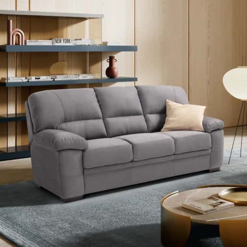 Divano 3 posti ESMI in tessuto grigio con cuscino beige, in soggiorno moderno con scaffali e lampada a terra.
