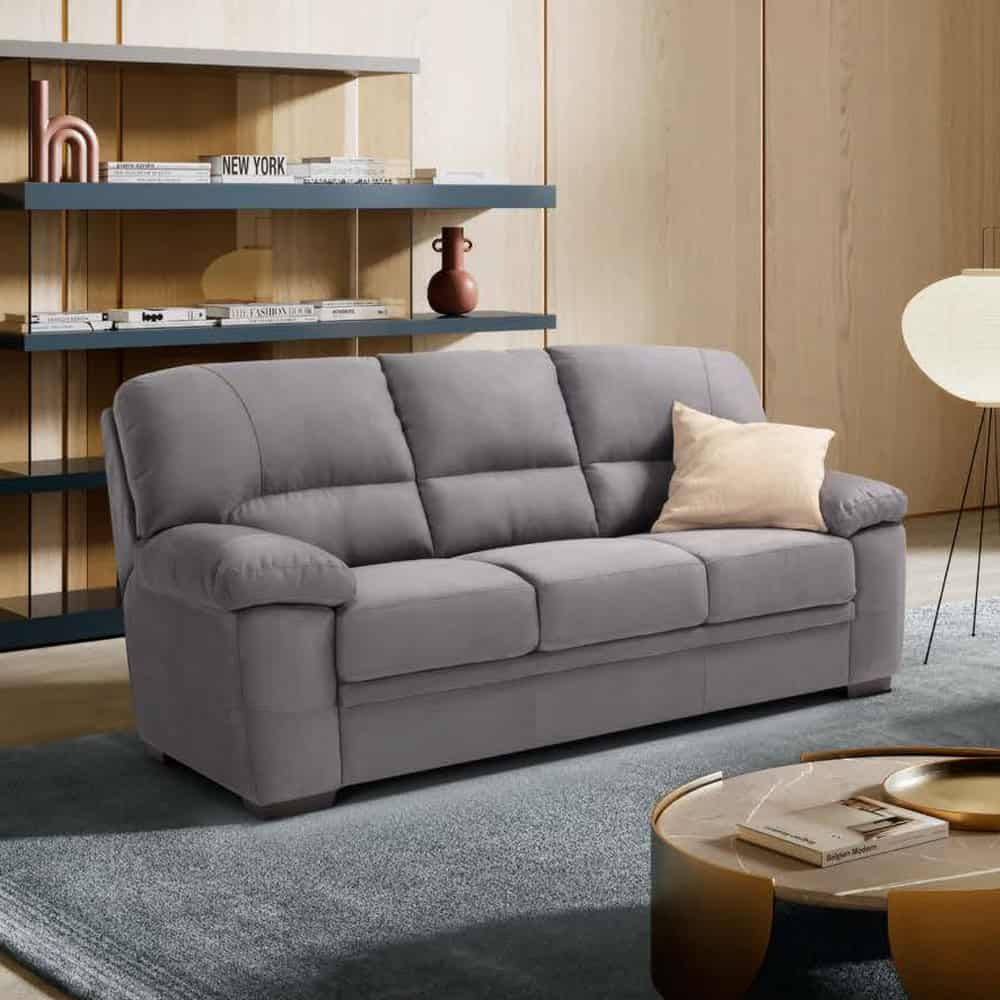 Divano 3 posti ESMI in tessuto grigio con cuscino beige, in soggiorno moderno con scaffali e lampada a terra.