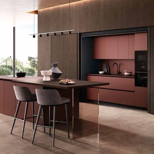 Cucina moderna con mobili in tonalità rosa e pareti in legno, con isola centrale e sedie grigie, ambiente luminoso e elegante.