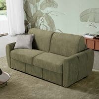 Divano modello Marte in tessuto verde oliva con braccioli arrotondati e cuscino grigio, in un soggiorno moderno con parete decorativa a foglie e finestra con tende bianche.