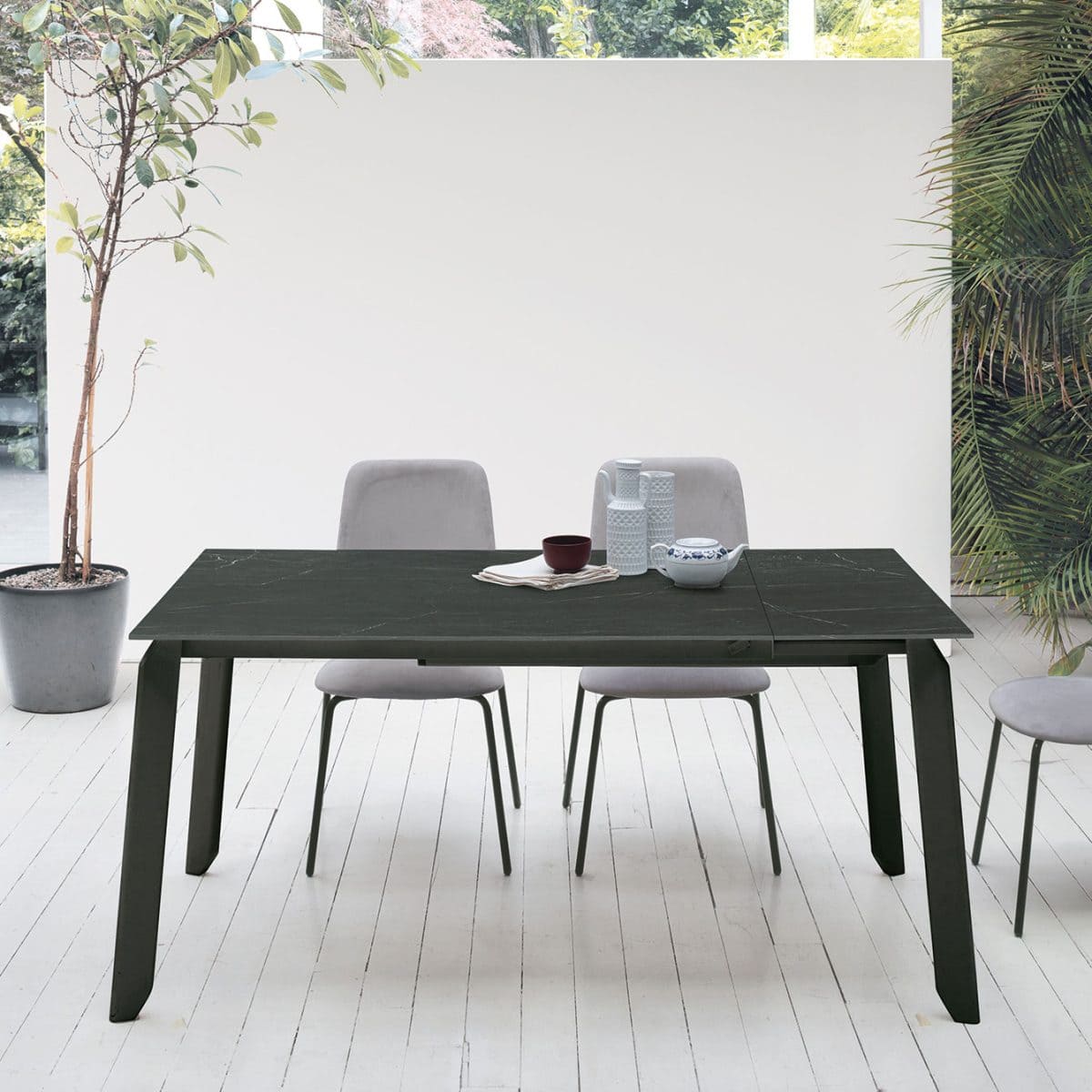 Tavolo EFESTO in legno scuro con sedie grigie in ambiente luminoso e minimalista, ideale per la zona pranzo di casa.