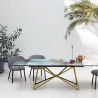 Tavolo moderno Galaxy con base gialla e piano in vetro, ambiente elegante con piante e arredi di design.