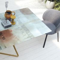 Tavolo GALAXY con superficie decorativa in stile moderno, abbinato a una sedia grigia, in un ambiente luminoso con piante verdi sullo sfondo.