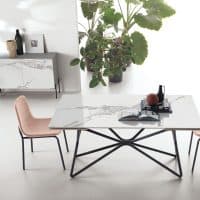 Tavolo Galaxy con piano in marmo bianco e struttura nera, ambientato in uno spazio minimalista con piante e arredi eleganti.