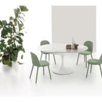 Tavolo JAZZ con sedie verdi in un ambiente minimalista, decorato con una pianta grande e un pannello bianco sullo sfondo.