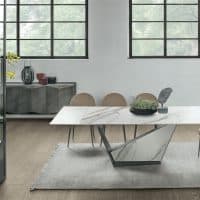 Tavolo moderno Galeone di Alpe Arredi con piano in marmo e base in metallo, in un ambiente luminoso con grandi finestre e sedie beige.