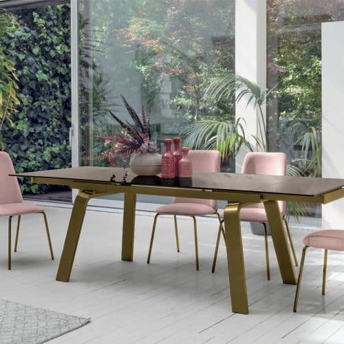 Elegante tavolo MARTE di Alpe Arredi con sedie rosa in un ambiente luminoso e moderno, circondato da piante verdi e grandi finestre che lasciano entrare molta luce naturale.
