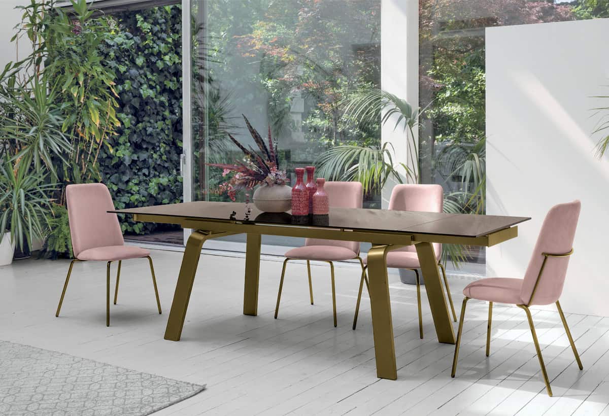 Elegante tavolo MARTE di Alpe Arredi con sedie rosa in un ambiente luminoso e moderno, circondato da piante verdi e grandi finestre che lasciano entrare molta luce naturale.