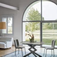 Elegante tavolo in gress con design moderno, ideale per ambienti living contemporanei, con grandi finestre che offrono vista sul verde esterno.