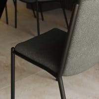 Sedia FUJI in tessuto grigio scuro con struttura nera in metallo, seduta imbottita e schiena leggermente inclinata sotto tavolo moderno.