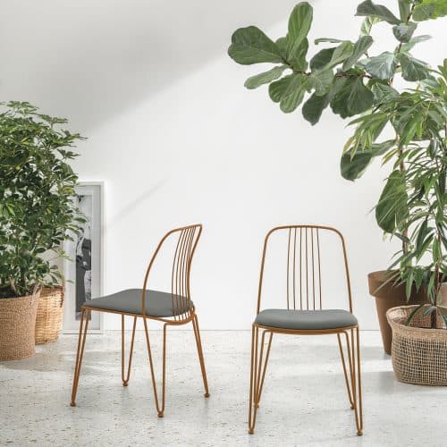 Due sedie Granada con struttura in metallo dorato e seduta grigia, all'interno di uno spazio luminoso con piante verdi e un pavimento chiaro, stile moderno ed elegante.