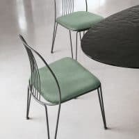 Sedia Granada in stile minimal con struttura metallica nera e cuscini verde salvia, tavolo nero circolare in un ambiente moderno.