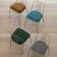 Set di quattro sedie Granada con gambe dorate e cuscini in velluto colorati, disposte su pavimento in legno.