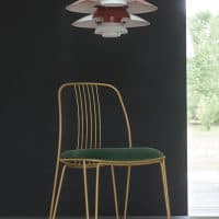 Sedia Granada con struttura in metallo dorato e schienale a barre, seduta in velluto verde, ambientazione moderna con lampadario colorato porzioni sovrapposte.