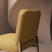 Sedia KANTO in tessuto senape con struttura metallica scura, sfondo arredamento moderno in tonalità neutre.