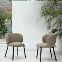 Due sedie KYOTO imbottite beige con gambe nere in ambiente luminoso, circondate da piante tropicali e pareti bianche, in stile moderno.