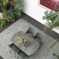 Tavolo TAY in pietra naturale con sedie moderne in un ambiente interno elegante e luminoso, circondato da piante verdi e decorazioni artistiche.